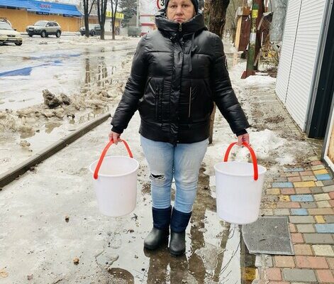 Photo was taken in Sviatohirsk, Donetsk Region. Olga, 55, a volunteer at the laundry set up by a CARE partner with her buckets.

80% of the buildings in town have been damaged or destroyed. There has not been any running water for nearly a year as the infrastructure has been severely damaged.
In Sviatohirsk a CARE partner has set up several water tanks to supply the residents with clean drinking water and water for showering, cleaning and cooking. Also a laundry was set up with the support of CARE, which is the only place in Sviatohirsk in which laundry washing is possible. Additionally, 40 houses have been repaired with the support of CARE and the renovation of another 325 is in process. Before the escalation of the war two years ago the village and surrounding settlements was home to 12,000 people. Now 2,700 remain of which 1,200 are elderly.

Olga, 55, is a volunteer at the laundry. They have 6 washing machines and 4 drying machines. The maximum of washing per day was 47 in the summer. Olga does not have a private water well in her own garden, so she needs to leave the house to gather the water for the day for her family.
“Every morning I get up at 8 a.m. to carry 150 liters of water to my house with buckets, because that’s what my family needs on a daily basis to cook, clean, shower or drink,” explains Olga.